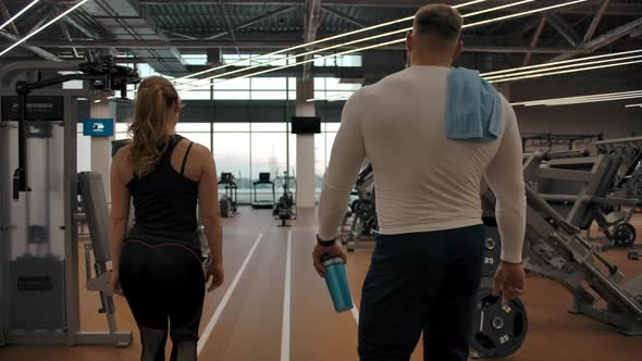 Couple of Athletes Go Through the Gym to the Exercise Machines