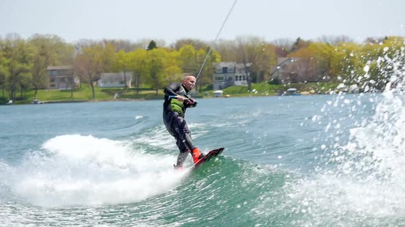 A man wakeboards behind a boat while wearing a wetsuit