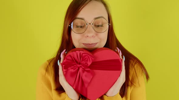 Woman in Glasses with Red Gift Box in Form of Heart on Yellow Background