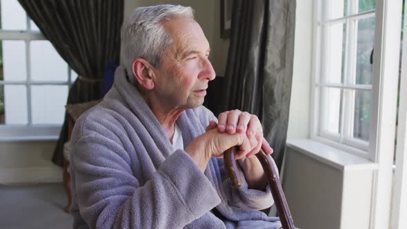 Sad senior caucasian man wearing bathrobe sitting by window