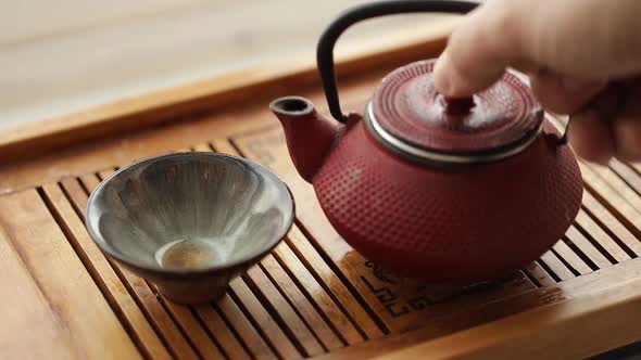 Tea is Poured Into a Bowl From a Red Chinese Teapot