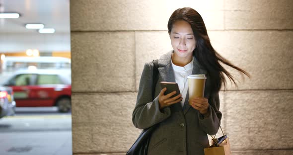 Businesswoman looking at cellphone and drink of coffee at night 