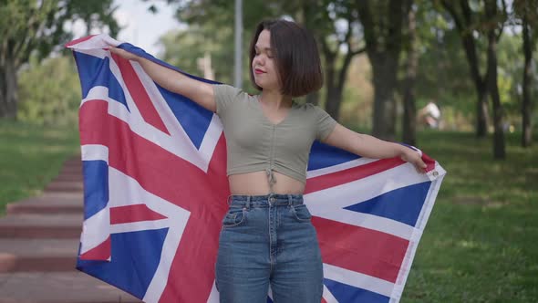 Medium Shot of Confident Smiling Little Person Stretching Hands with British Flag Standing in Park
