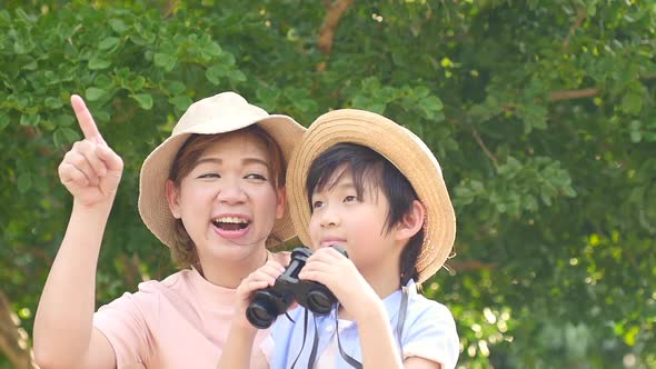 Asian Mother And Her Son Using Binocular And Pointing On Summer Day