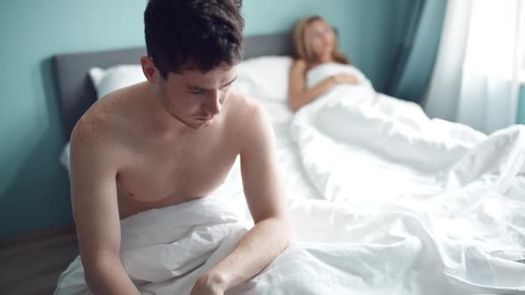 Frustrated Man Sitting on Bed on Different Side of Woman