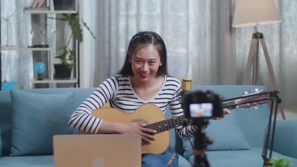 Woman With A Laptop Waving Hand And Speaking To Camera While Live Stream Playing A Guitar At Home