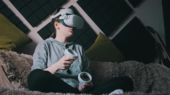 Young Woman Sitting on Sofa Playing Game Using VR Helmet Indoor at Home