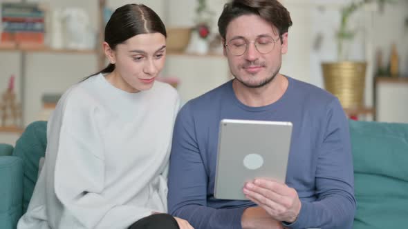 Hispanic Couple Doing Video Call on Tablet While Sitting on Sofa