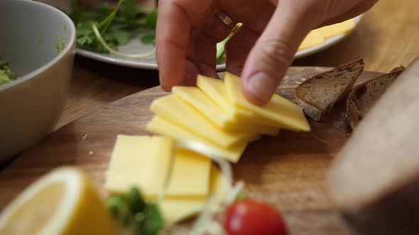 Side View of Hands Arranging Breakfast Board. Placing Yellow Cheese on Wooden breadboard.Healthy