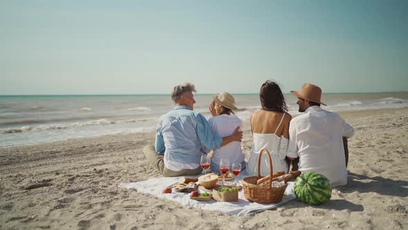 Slow Motion Rear View Four Happy Friends Wto Couples Sitting on Picnic Blanket with Food 