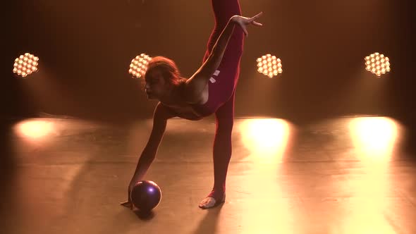 Sports Girl Gymnast Performs Acrobatic Exercises with Ball and Does Stretching, Showing the