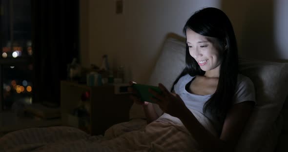 Woman use of mobile phone on bed at night 