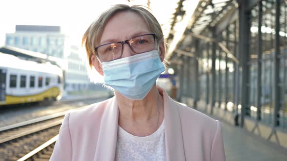 Portrait of an Elderly Woman in a Medical Mask on Her Face Standing on the Platform Waiting for His