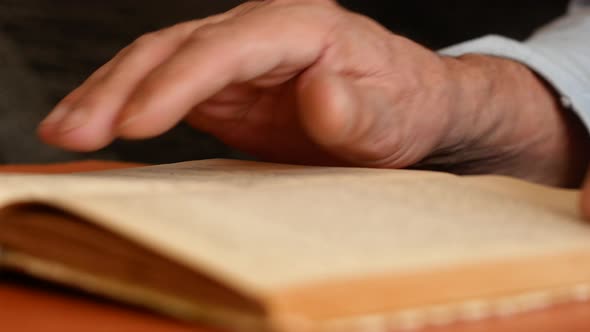 Close-up of an open old book in the hands of an elderly man.
