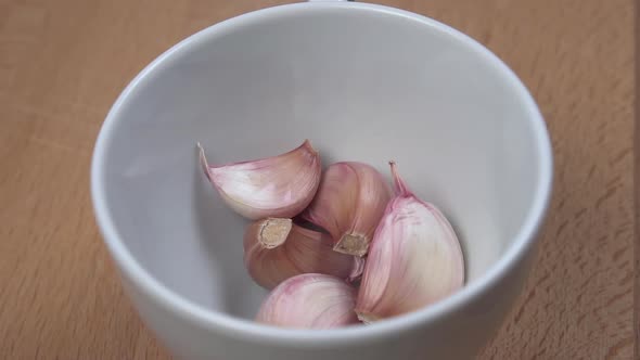 Garlic cloves fall into a white cup close-up on a cutting board. 