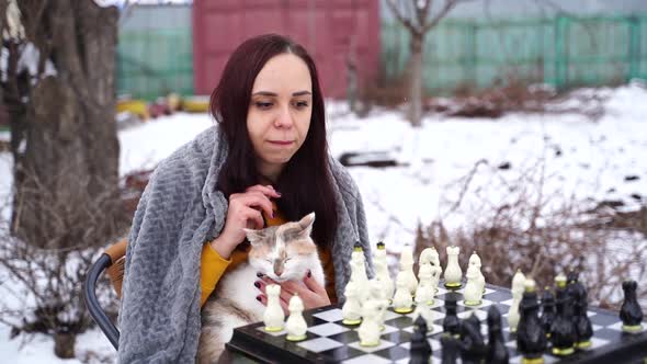 Young Woman Sitting with Cat and Playing Chess in Yard