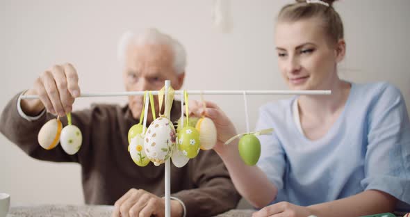 Senior Man and Granddaughter Decorating Table With Easter Eggs and Easter Decorations.