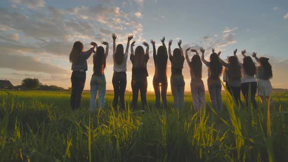 Silhouette of Friends of 11 Girls Waving Their Hands at Sunset in the Field