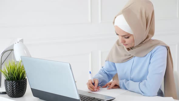 Young Muslim Woman Student in Hijab is Doing Her Homework Writing and Drawing Table on Paper Using