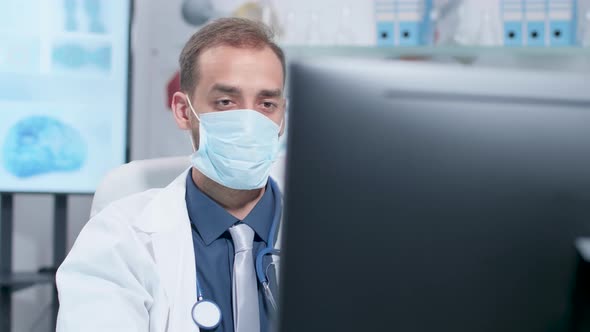 Handheld Shot of Doctor Wearing a Medicinal Mask Working on the Computer