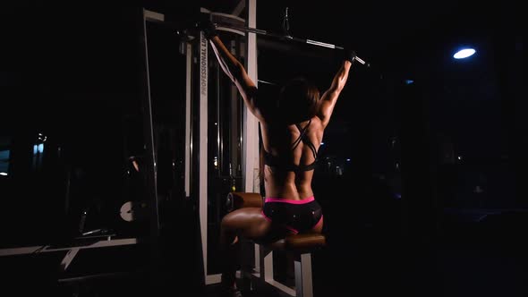 A Strong Muscular Athletic Bodybuilder Girl in Short Shorts Trains the Back Muscles on a Horizontal