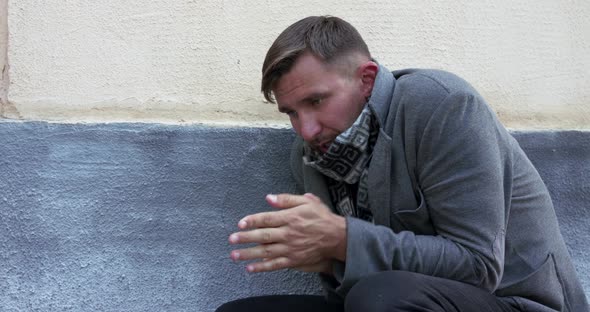 Portrait of Sitting Down Man Suffers From Severe Fever at Street Building