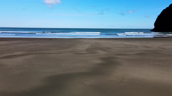 Flying across the textures of Piha black sand beach and into the famous surf break