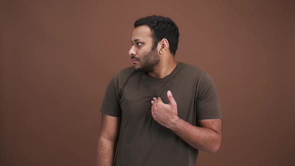 Puzzled Indian Man Looking Around with Misunderstandment Saying It's Not Me Brown Studio Background