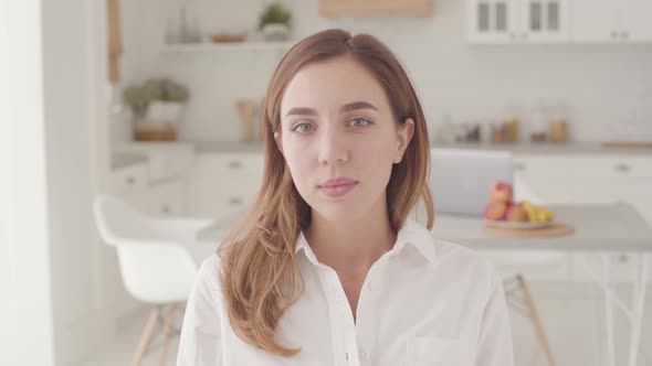 Portrait of a Young Smiling Caucasian Girl Sitting in Light Modern Kitchen