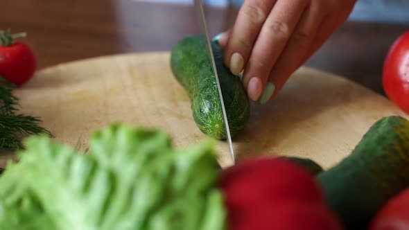 Closeup of a Woman Cuts in Half with a Knife Fresh Cucumber on a Cutting Board