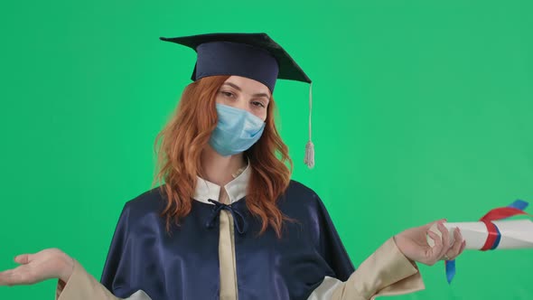 Adult Female Student in Medical Mask and an Academic Gown and Hat with Diploma Spreads Arms to Side