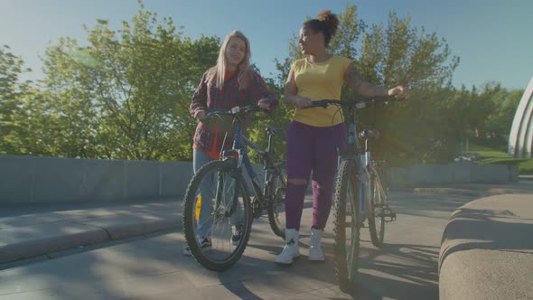 Multiethnic Lovely Women with Bicycles Walking in City at Daybreak