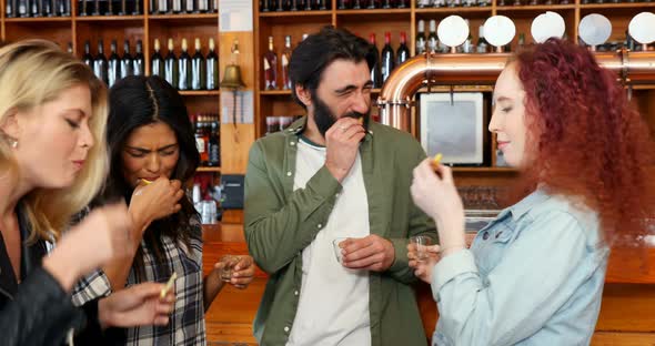 Friends having tequila shot at counter in bar 4k