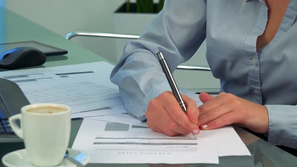 A Woman Writes on Papers in an Office - Closeup on the Hands