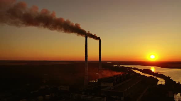 Dark smoke goes from industrial pipes at sunset