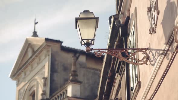 Traditional old street lamp on a building wall, with a church in the background, Bracciano town, Ita