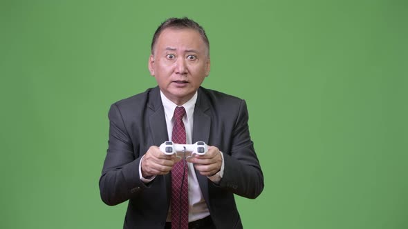 Mature Japanese Businessman Playing Games Against Green Background