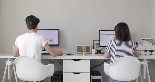 A couple of freelancers In the home Office. Sitting at the white Desk and Working on computer.