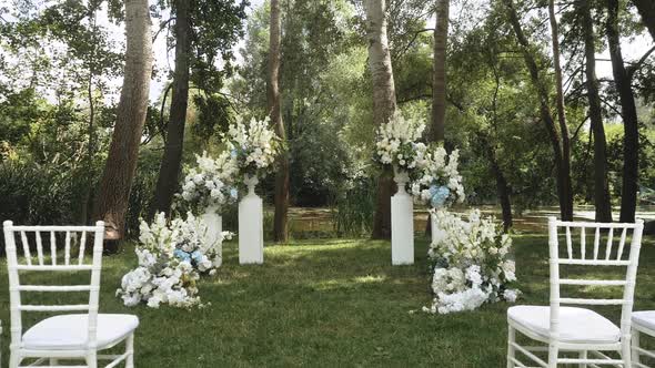 Wedding Arch Decorated with Pastel Faded Flowers and White Chairs Lake on the Background Slow Motion
