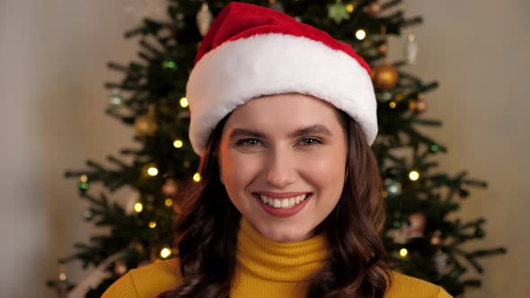 Close Up Smiling Young Woman Wearing Santa Claus Hat Looks Camera at Home