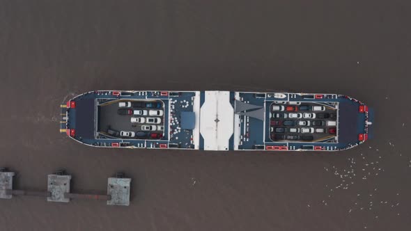 Overhead top down aerial drone shot of car ferry leaving docks fully loaded seagulls swarming