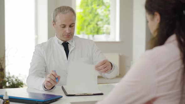 Portrait of Serious Mid-adult Doctor Looking Through Patient's Examination Results and Shaking Head