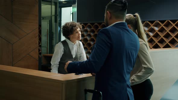 Hotel Receptionist Talking To Guests Giving Key Cards Welcoming Customers Standing at Reception Desk