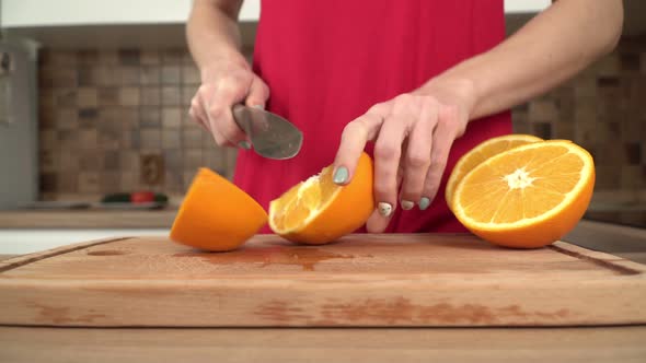 A Woman is Cutting a Juicy Orange in the Kitchen Closeup