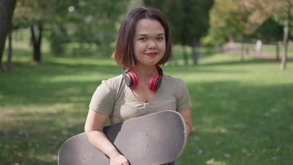 Medium Shot Portrait of Charming Young Woman with Dwarfism Posing in Park with Skateboard