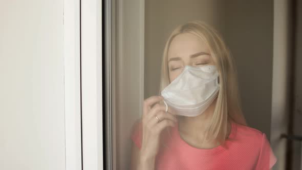 Young Beautiful Girl Removes a Medical Mask Standing at Window.