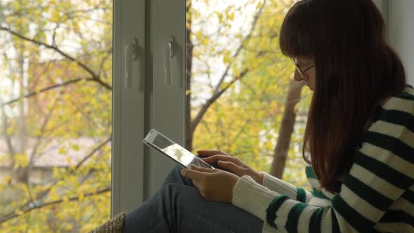 Girl Sitting on the Sill in the Street Yellow Leaves and Reads on the Internet.