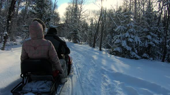 Snowmobile with Two People Riding Through Winter Forest at Cold Sunny Day Pov