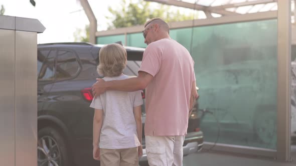 Back View Man Hugging Boy Talking Standing at Clean Vehicle at Car Wash Service Outdoors