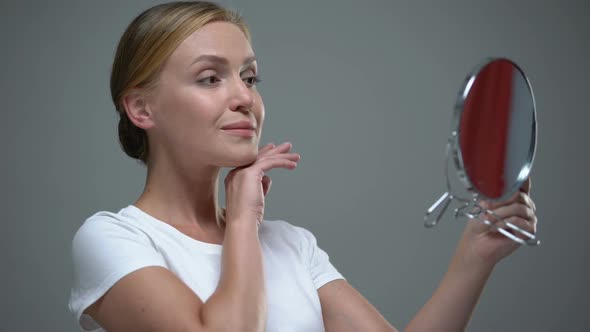 Attractive Lady Admiring Her Beauty Looking in Mirror, Anti-Aging Cosmetics
